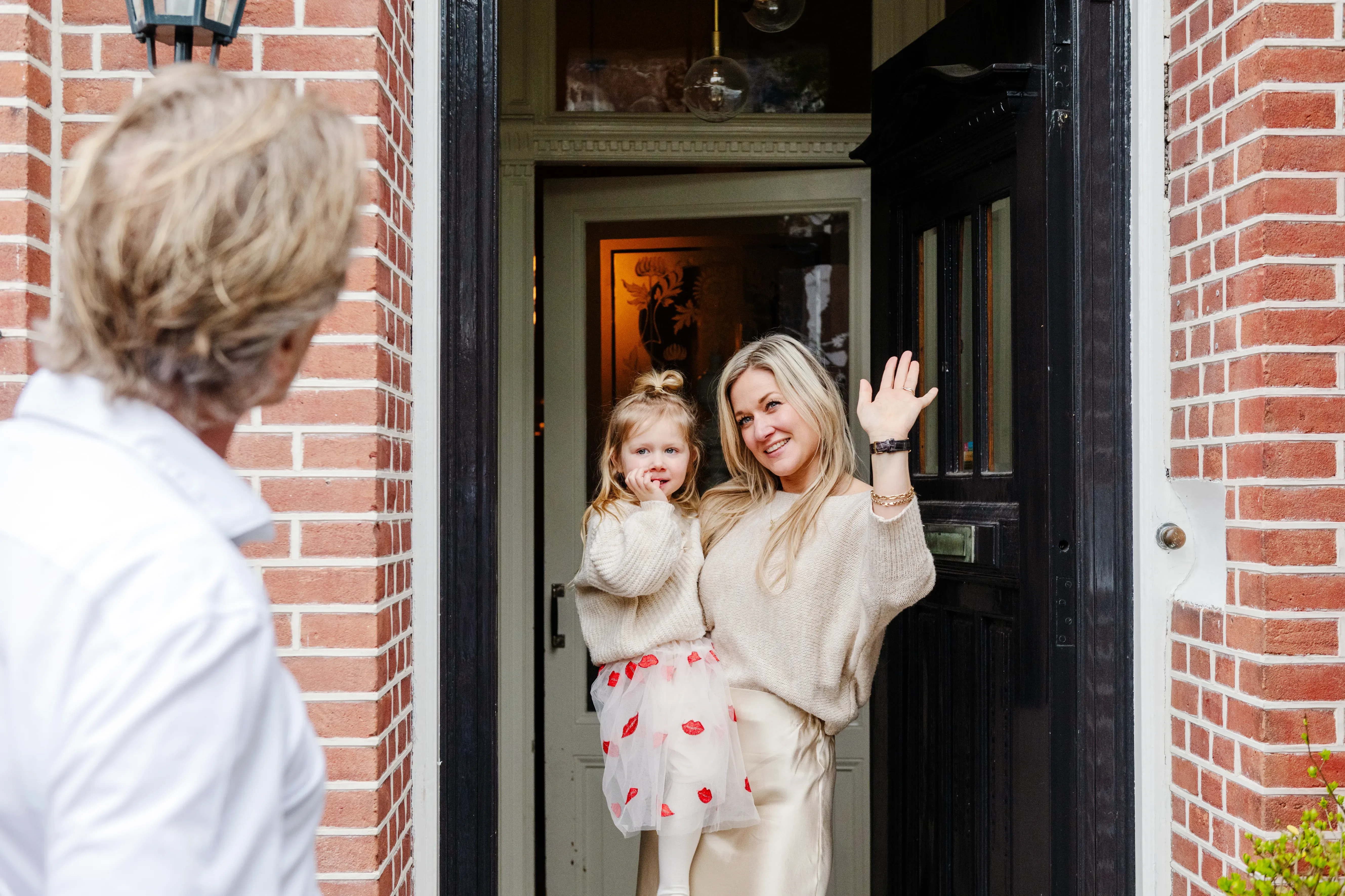 Vrouw met kind in haar armen, zwaaiend naar haar man