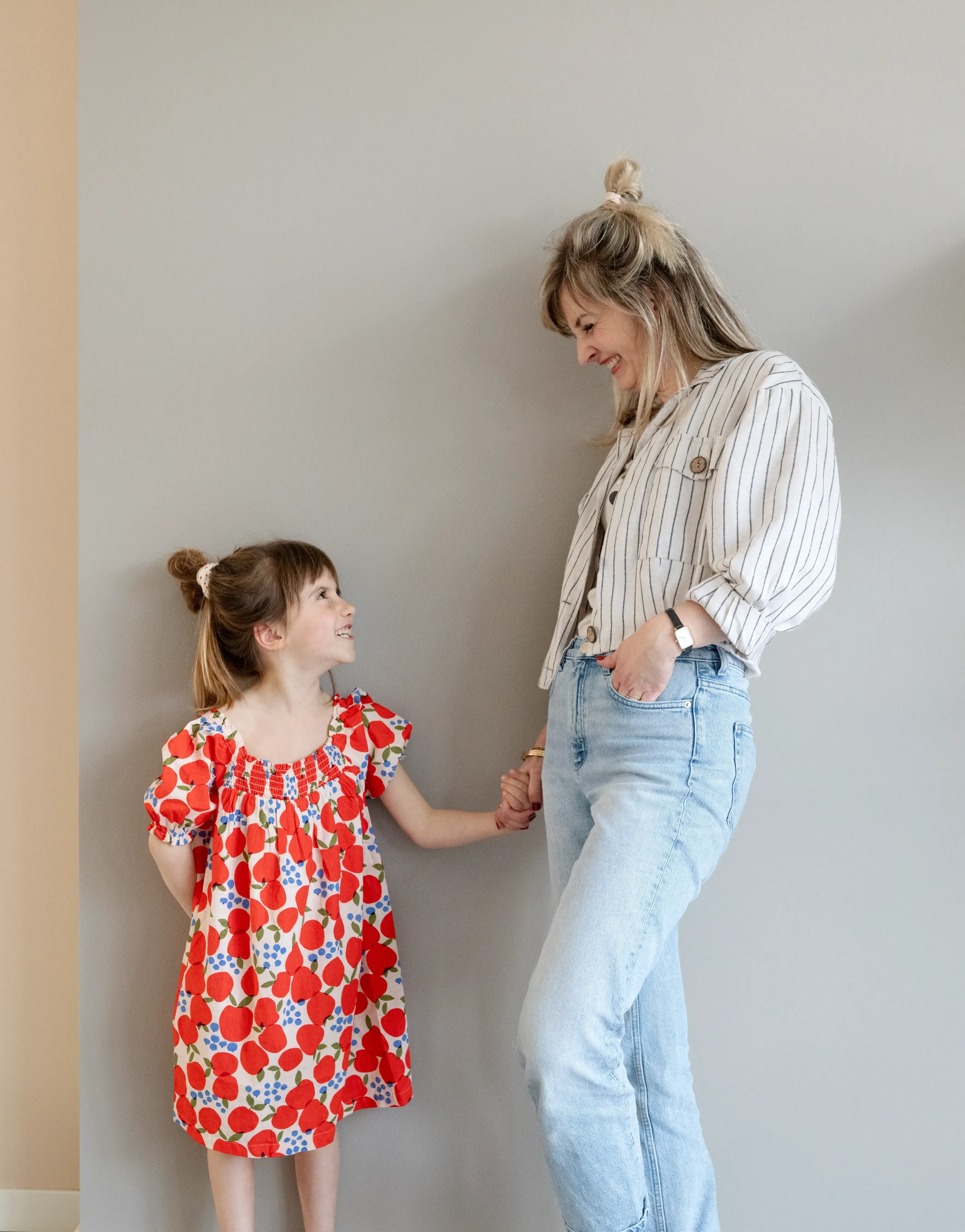 Moeder en dochter lachen naar elkaar en hebben hand vast tegen een muur aan