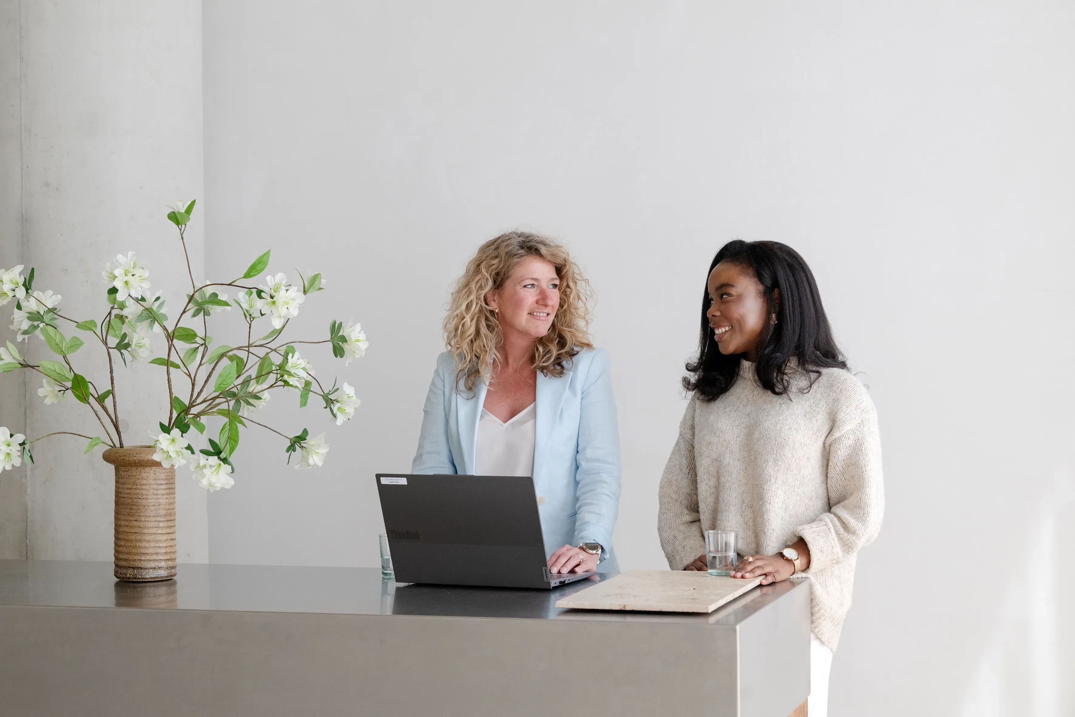 Twee vrouwen staan achter laptop lachend naar elkaar