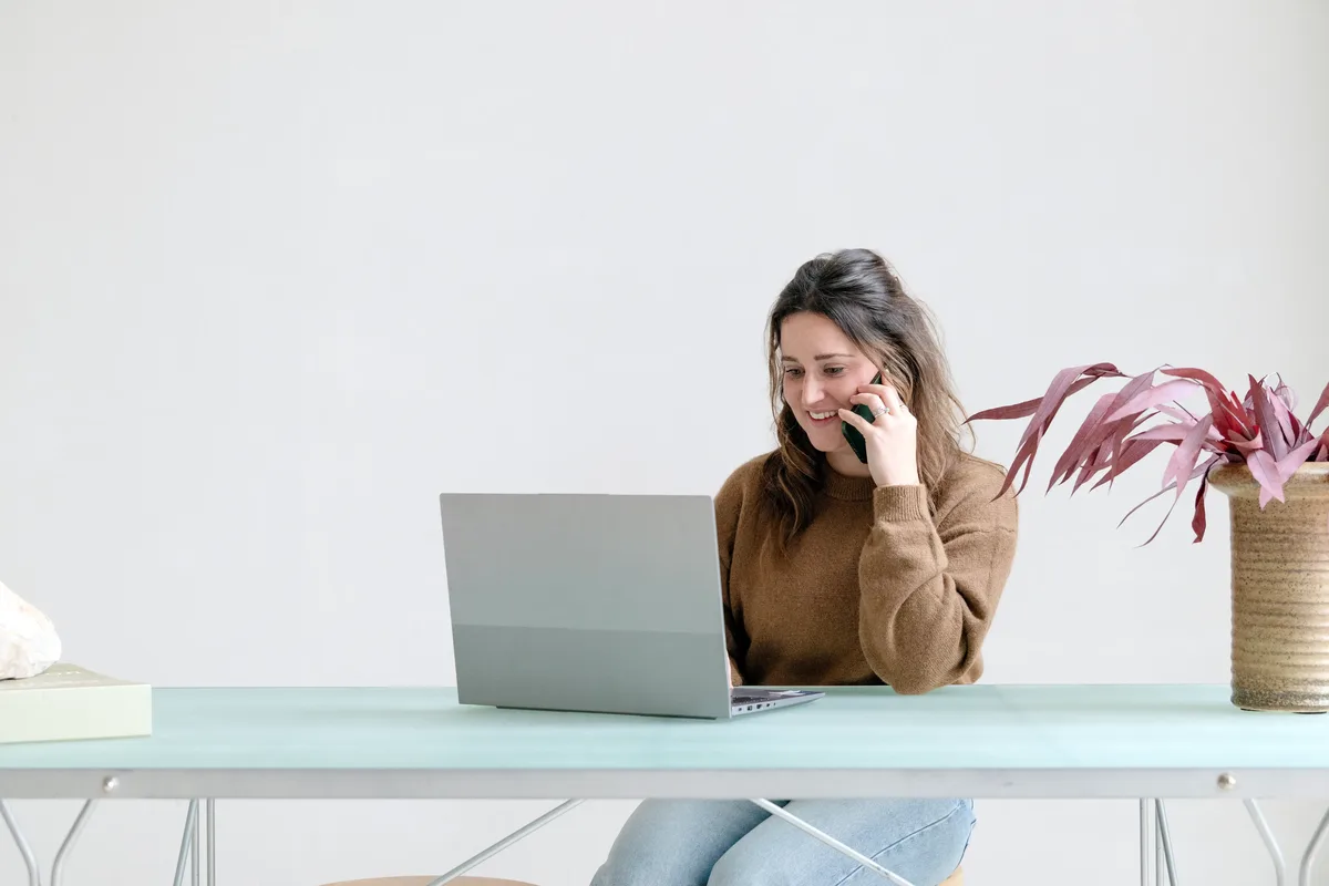 Vrouw aan het bellen en kijkt naar laptop