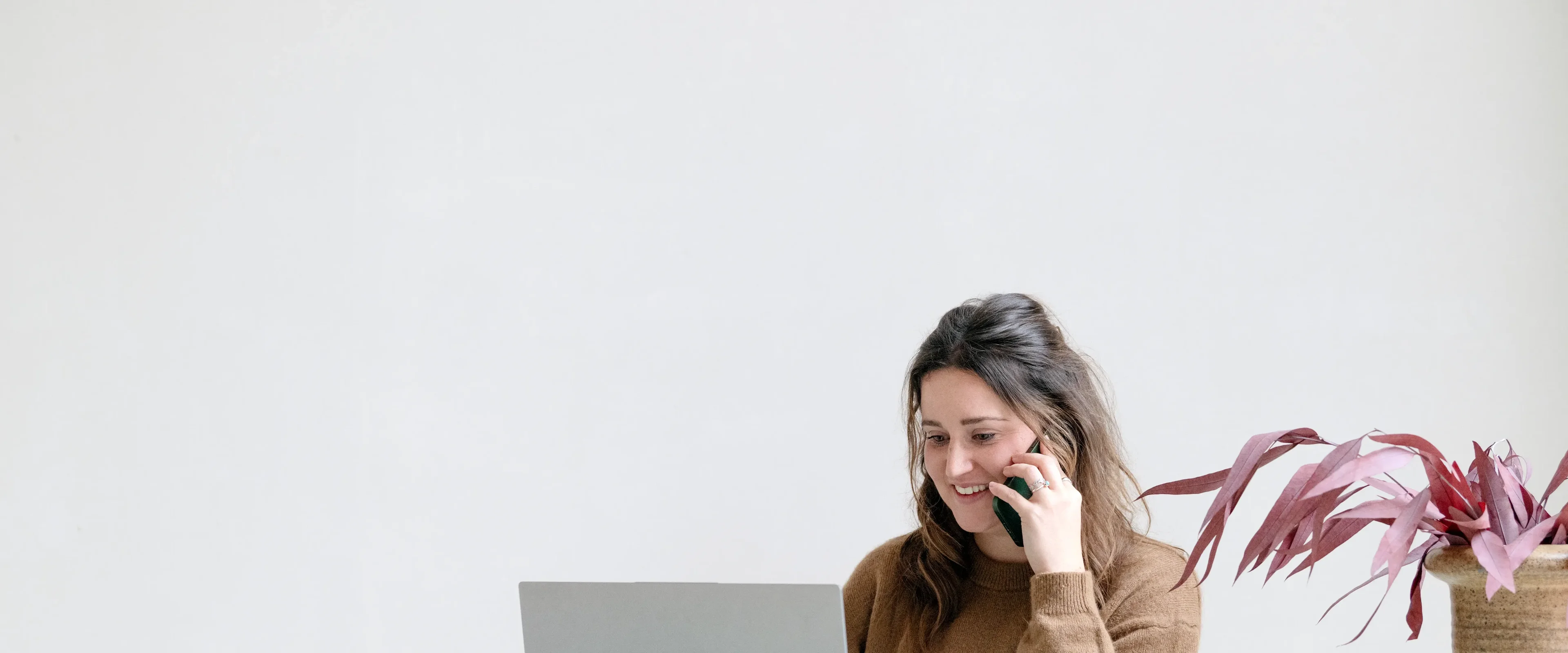 Vrouw aan tafel, bellend achter haar laptop