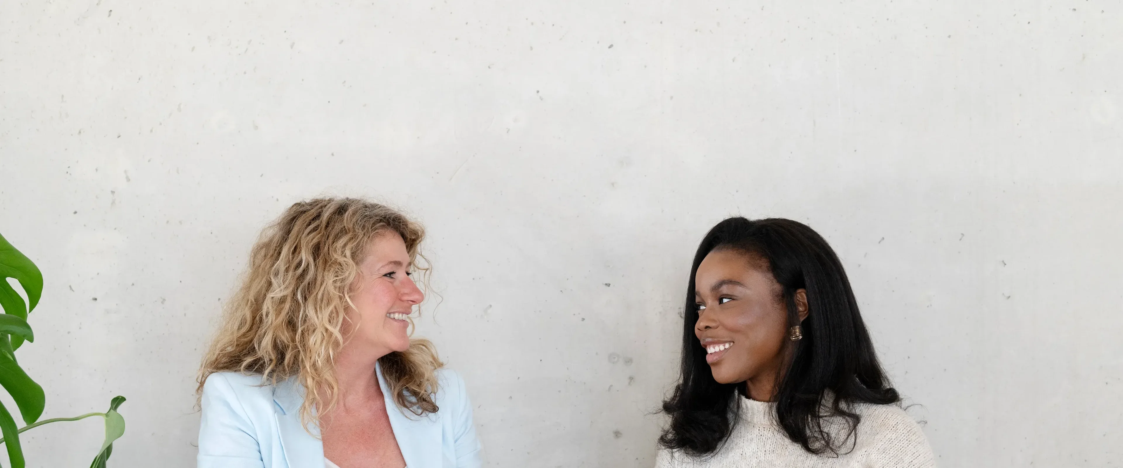Twee vrouwen aan tafel glimlachend naar elkaar