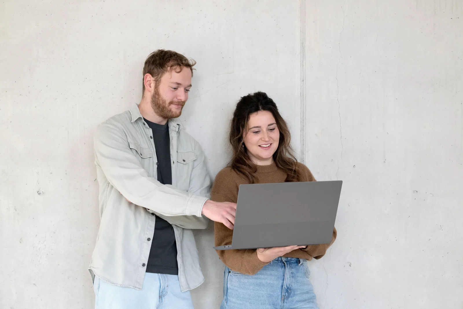 Man en vrouw leunend tegen muur kijken naar laptop